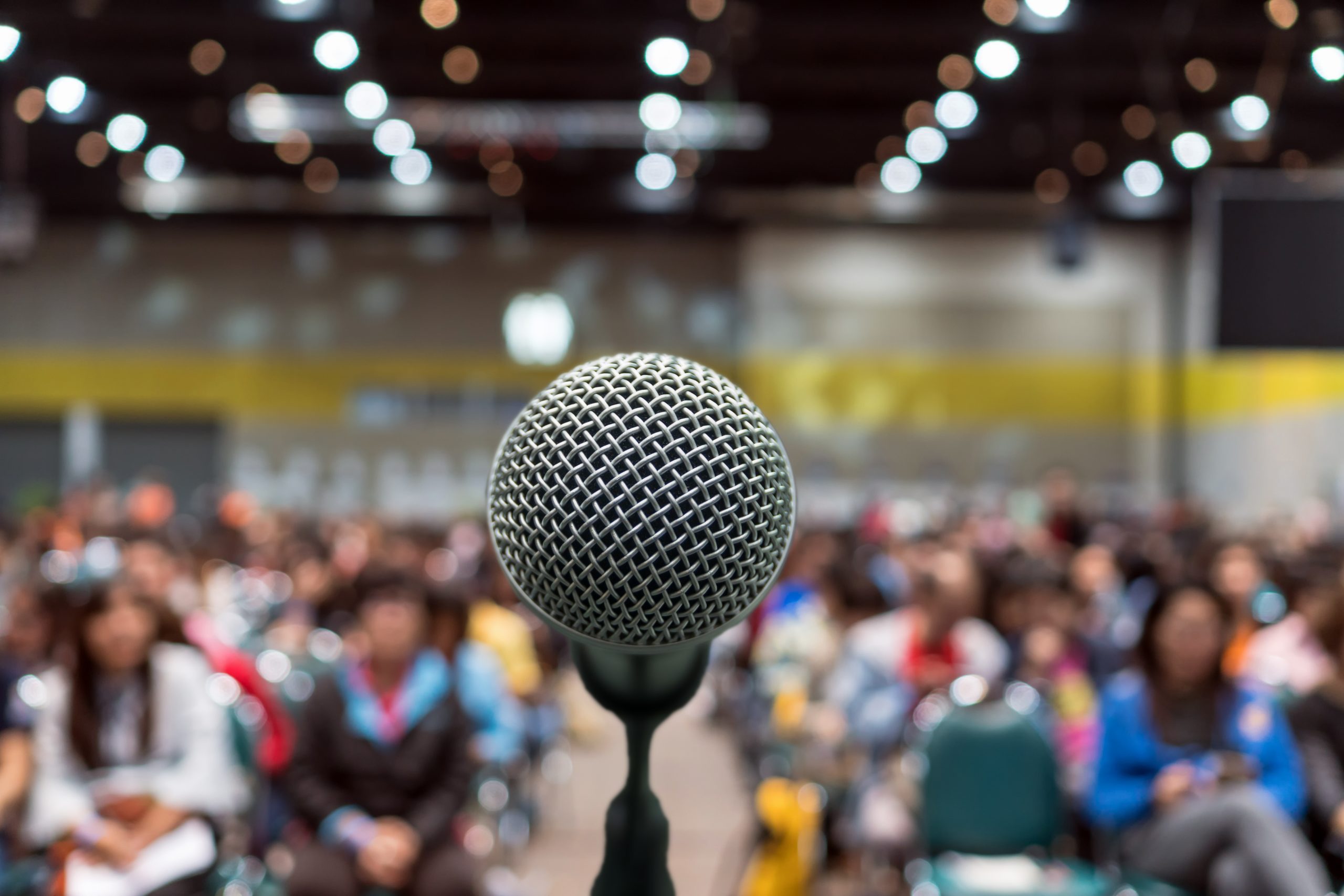 Microphone Over The Abstract Blurred Photo Of Conference Hall Or
