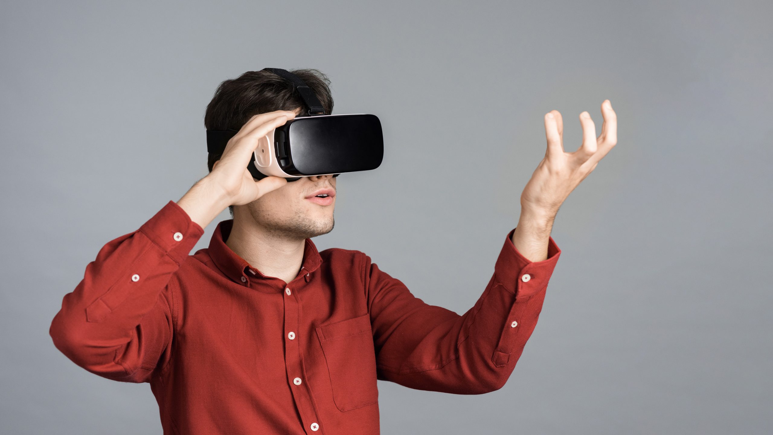 A Young Man Is Playing Games Using Vr Glasses, Holding A Virtual Thing, Gray Background